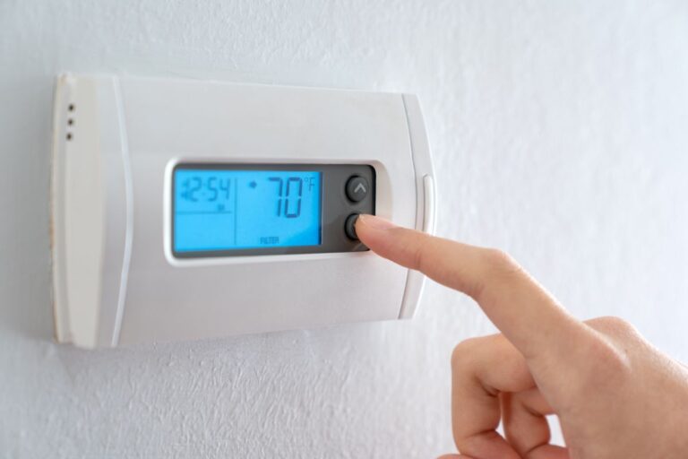 A woman is pressing the down button of a wall attached house thermostat with digital display