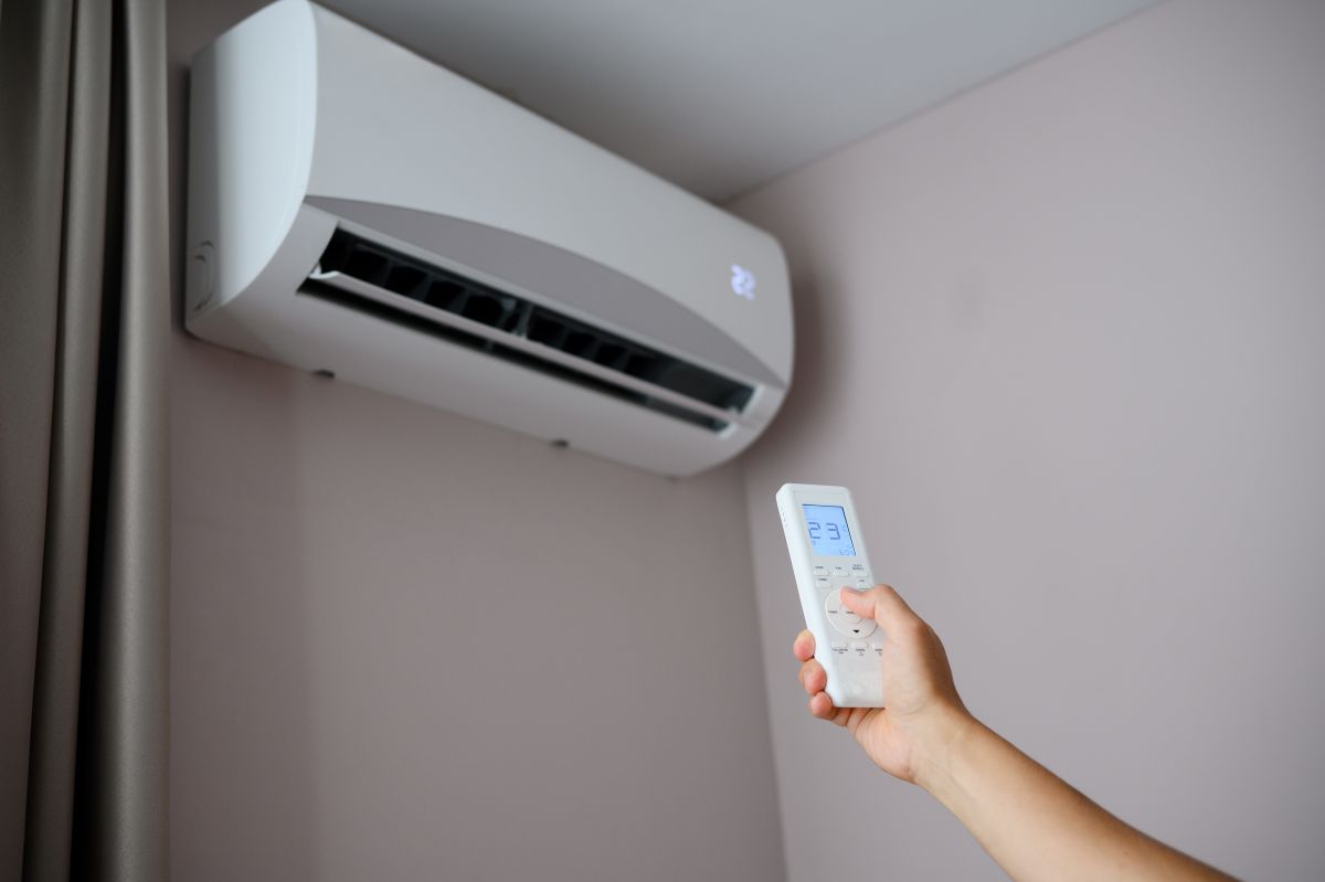 Man holds remote control in front of an air conditioner, adjusting its temperature